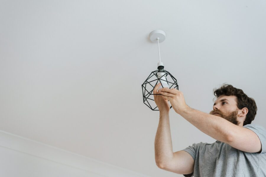 A man changing a light fixture with a bottom-up view of him doing so.