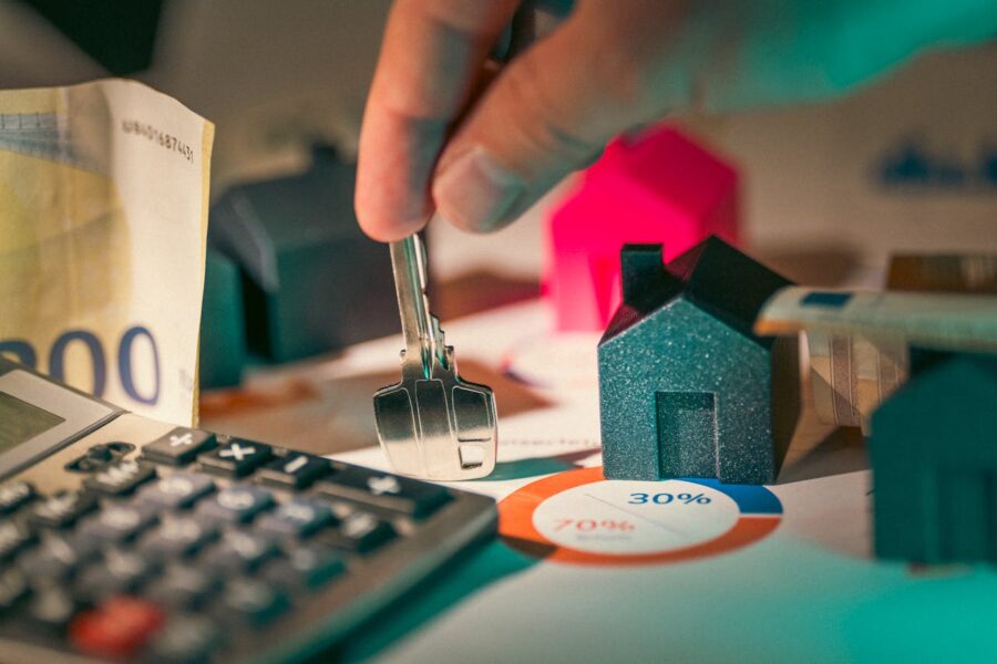 A person holding a key next to a calculator, model houses, money, and graph.